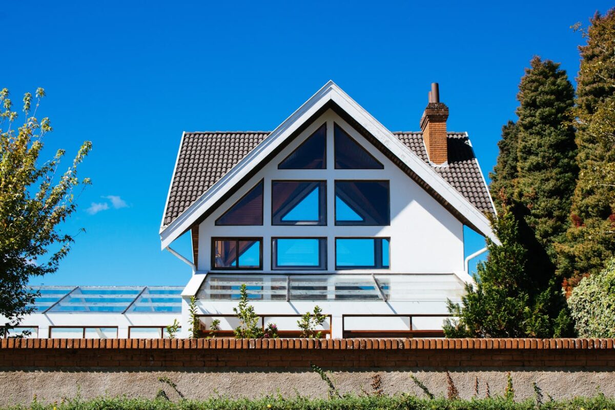 Contemporary A-frame house with large glass windows on a sunny day, surrounded by greenery.